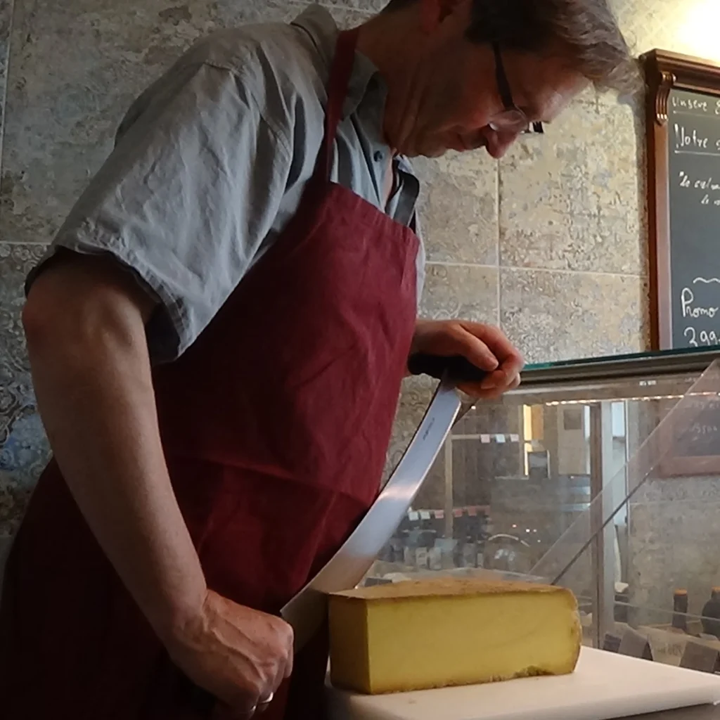 Chez Martin Ihre Käse- & Weintheke in Potsdam-Babelsberg. Authentisch. Ausgewählt. Einzigartig. - Mitarbeiter schneidet großen frischen Käselaib