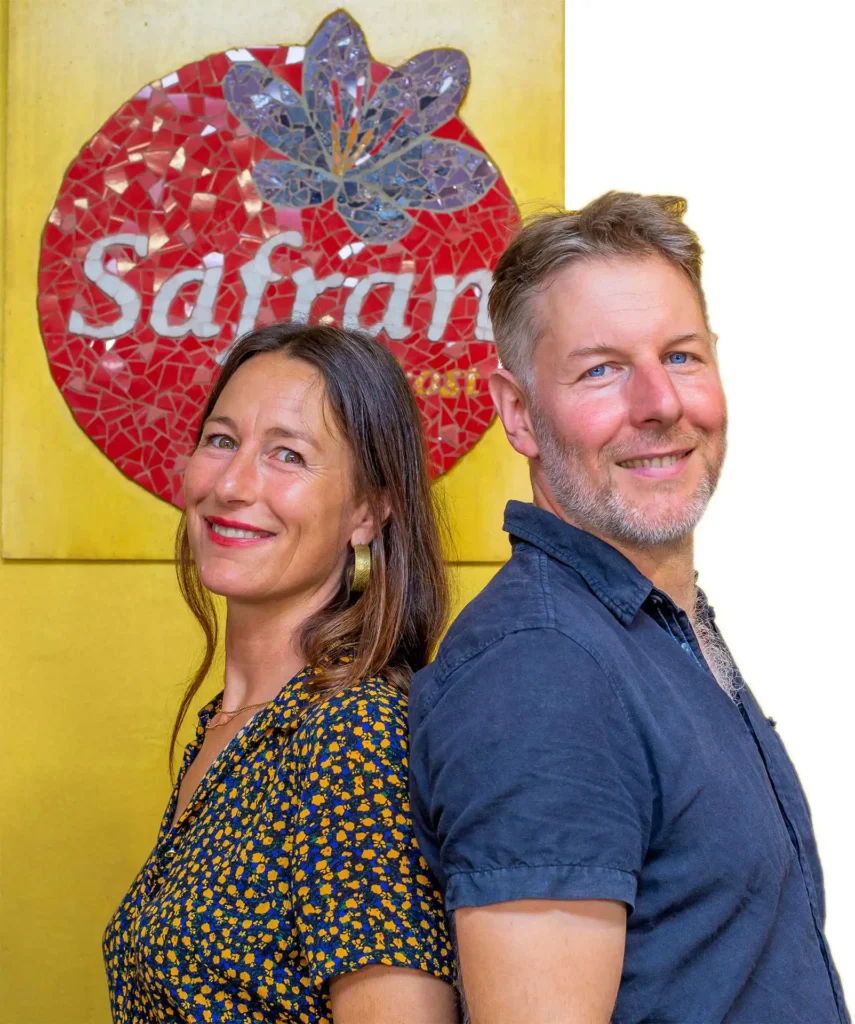 Safran Naturkost Ihr Bioladen mit Charme. Herr Sylvain Durand Inhaber und Geschäftsführer mit seiner Mitarbeiterin lachend vor dem Logo im Laden