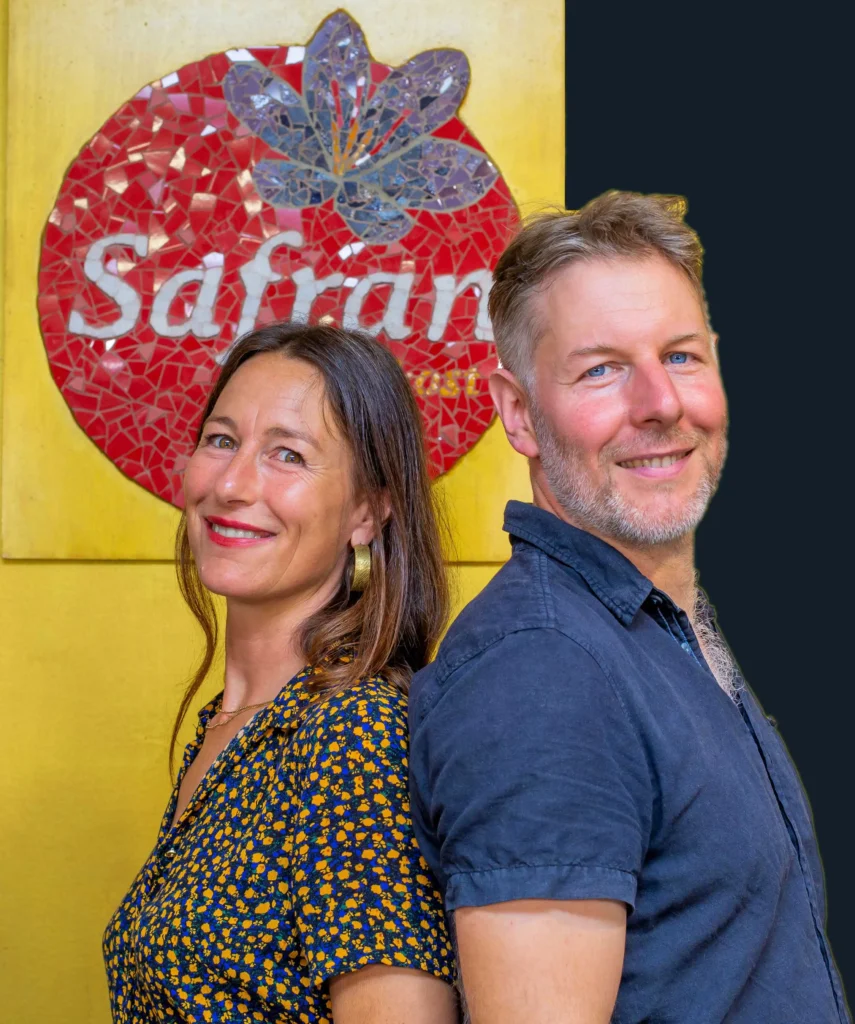 Safran Naturkost Ihr Bioladen mit Charme. Herr Sylvain Durand Inhaber und Geschäftsführer mit seiner Mitarbeiterin lachend vor dem Logo im Laden